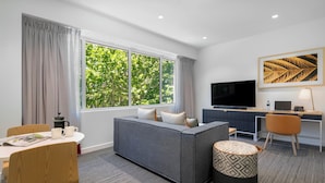 A modern hotel room with a grey sofa, a dining table with chairs, a TV, and a desk with a computer. - Quest Canberra City Walk (Canberra)