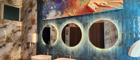 A bathroom with three sinks, marble walls, and a large abstract painting above the mirrors.