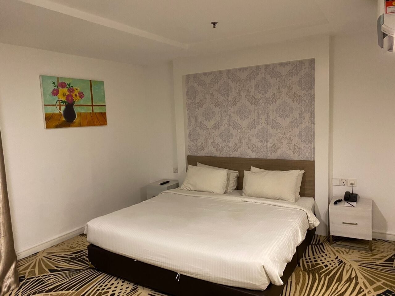 Una habitación de hotel con una cama grande, una mesita de noche, un teléfono en la pared y un cuadro colgado.