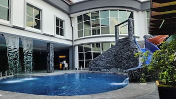 A pool area with a slide, a stone waterfall feature, and a seating area with a table and chairs.