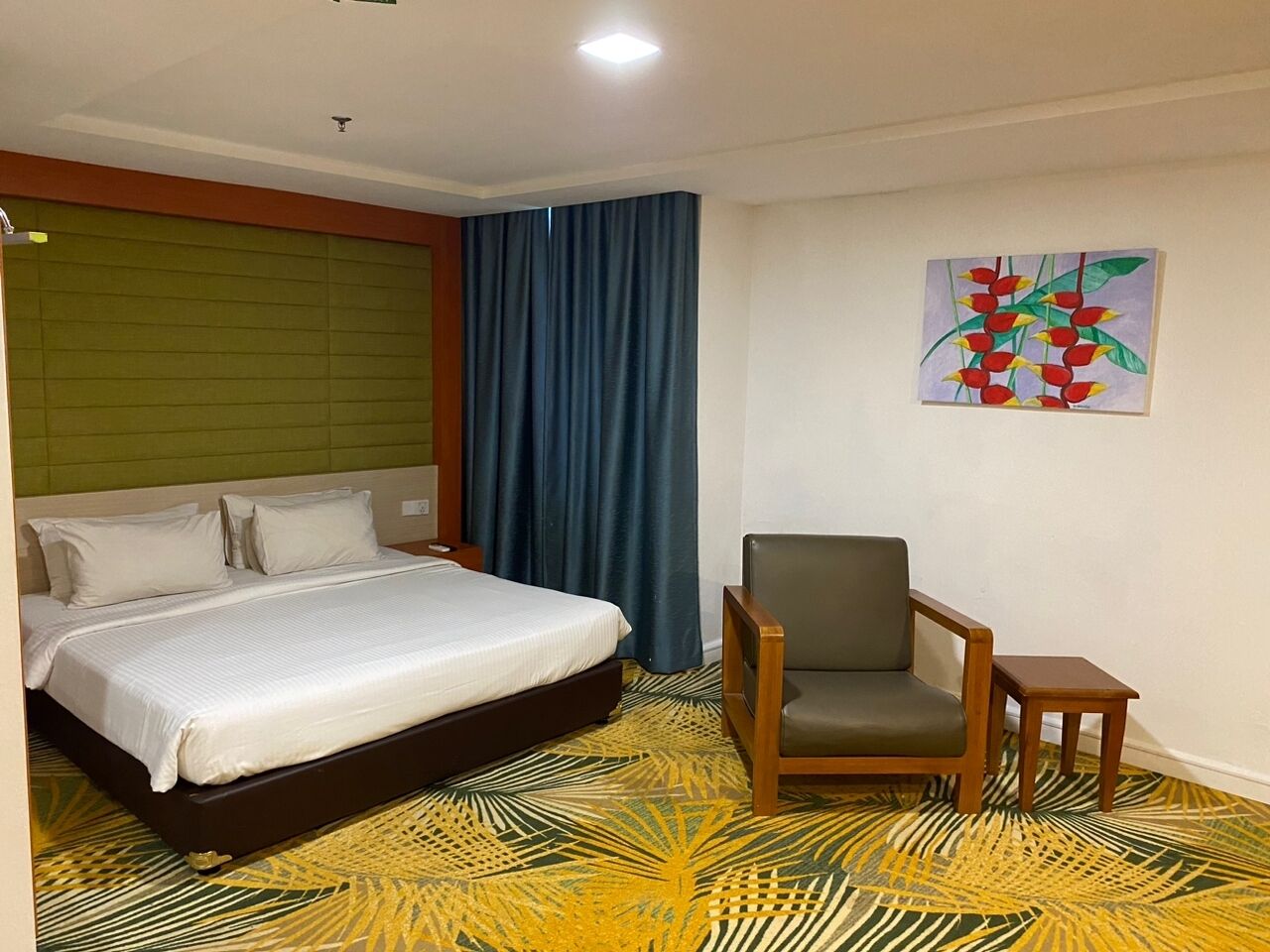 A hotel room with a bed, a chair, a small table, and a painting on the wall.