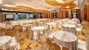 A large banquet hall with round tables covered in white tablecloths and chairs, a stage with a presentation screen, and a decorative ceiling light fixture. - De Palma Hotel Shah Alam (Shah Alam)
