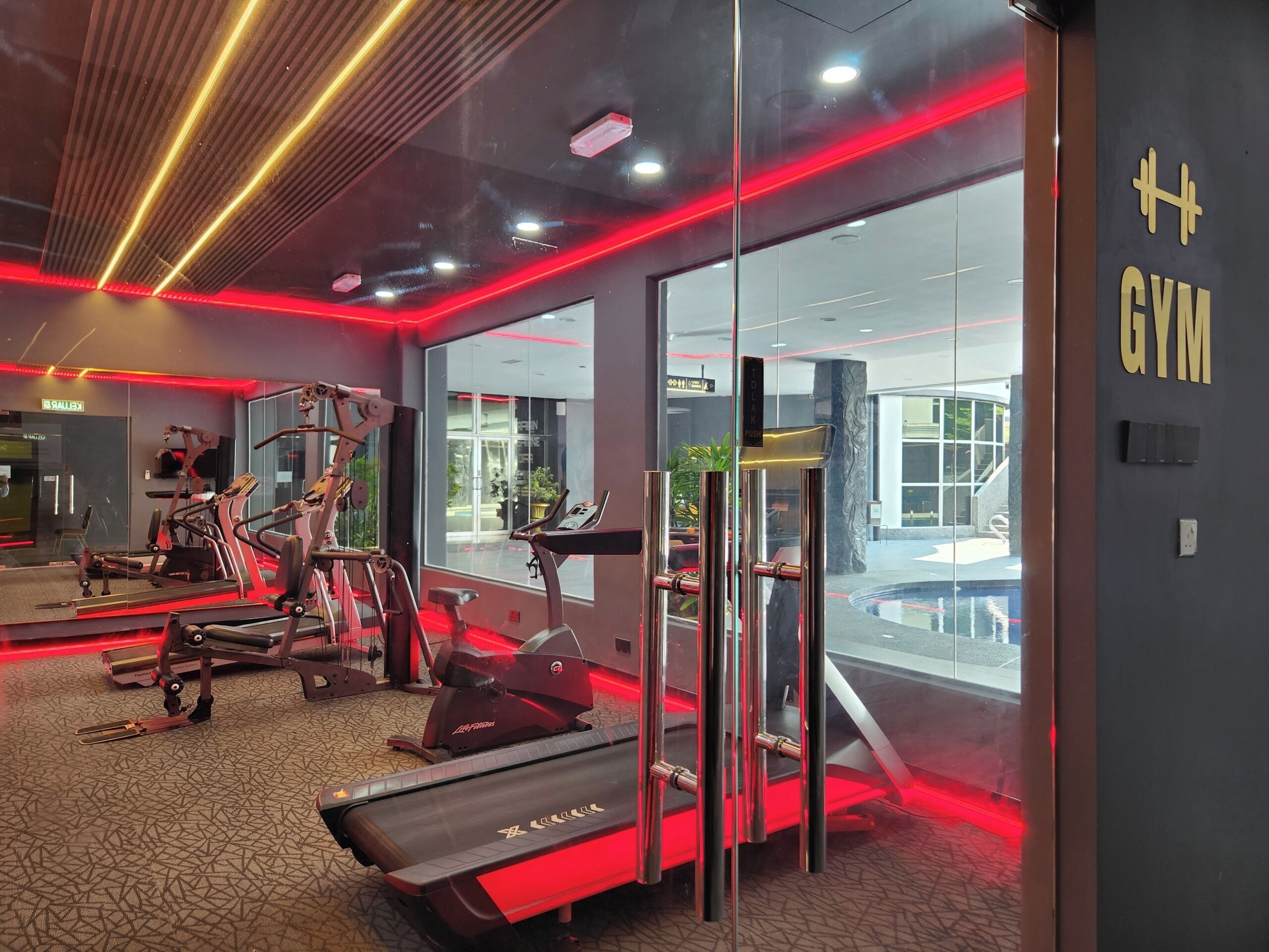 Academia moderna com equipamentos de exercício, parede de vidro e placa indicando ser uma academia.