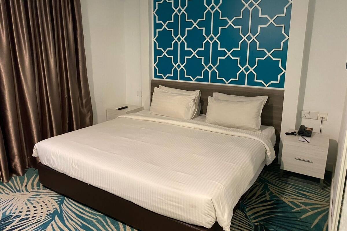 Une chambre d’hôtel avec un grand lit, une table de chevet avec un téléphone et un panneau décoratif au mur.