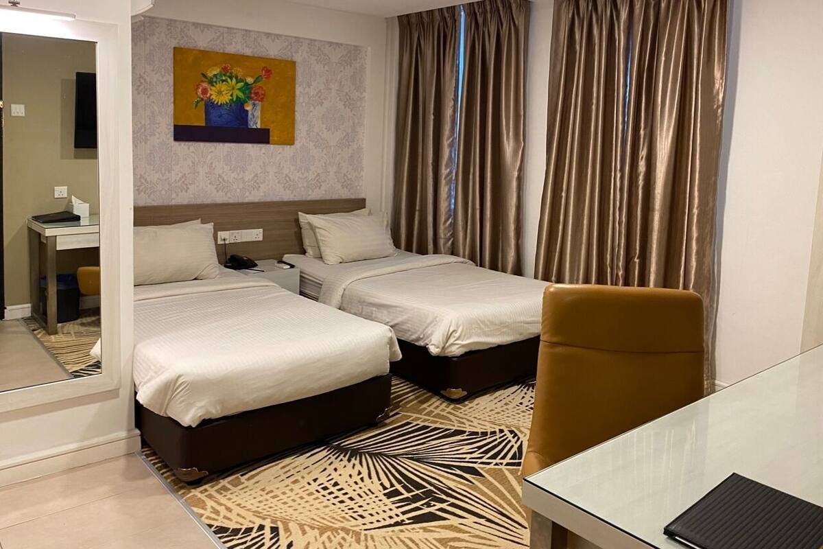 Une chambre d’hôtel avec deux lits, un bureau, une chaise, un tableau au mur et un tapis à motifs.