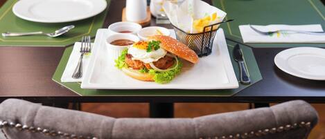 A dining table set with a burger, condiments, and a basket of fries.