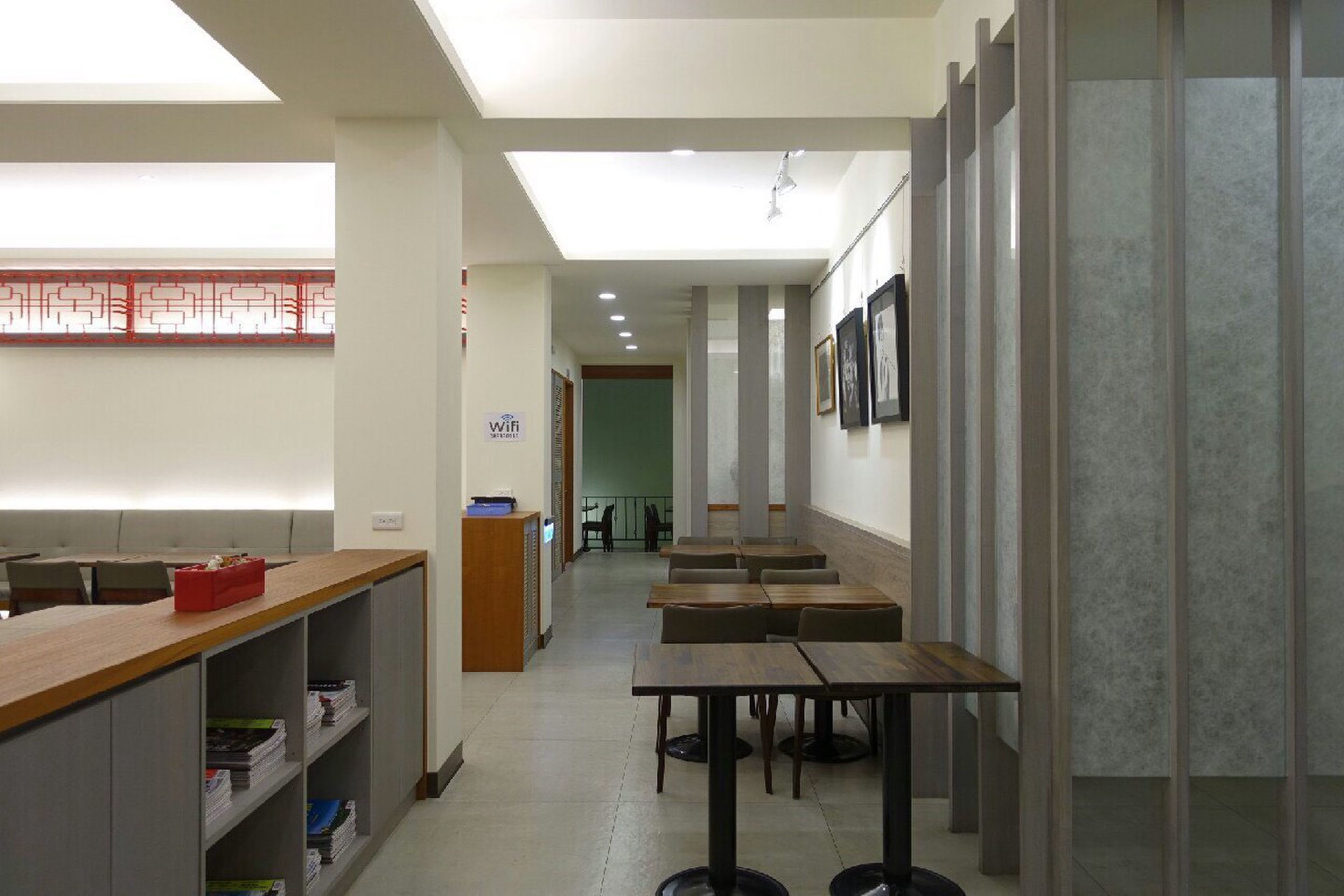 A modern hotel lobby with a reception desk, seating area, and a staircase leading to the upper floor.