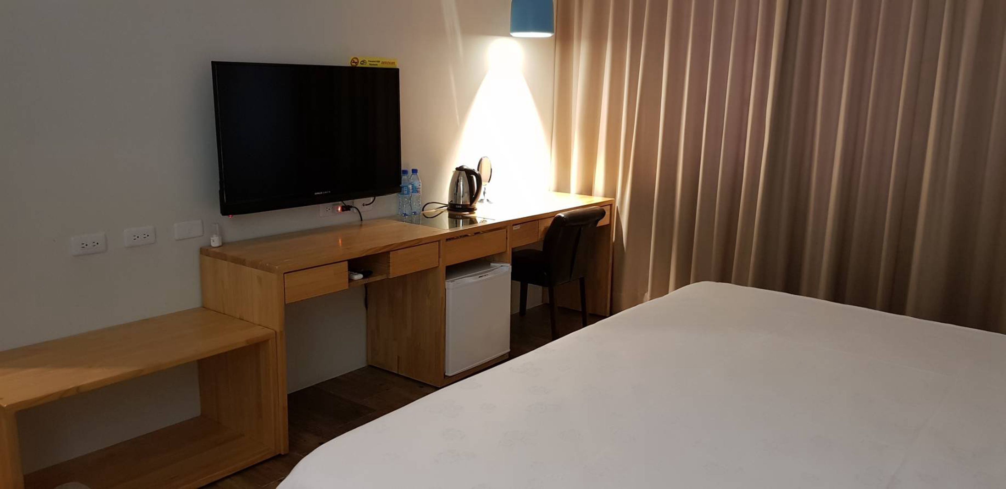Una camera d'albergo con un letto, una scrivania con un computer, una televisione e un piccolo frigorifero.