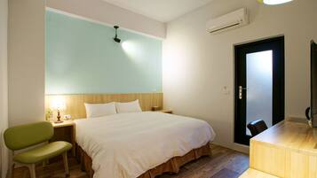 A hotel room with a bed, a desk, a chair, a lamp, and an air conditioning unit.