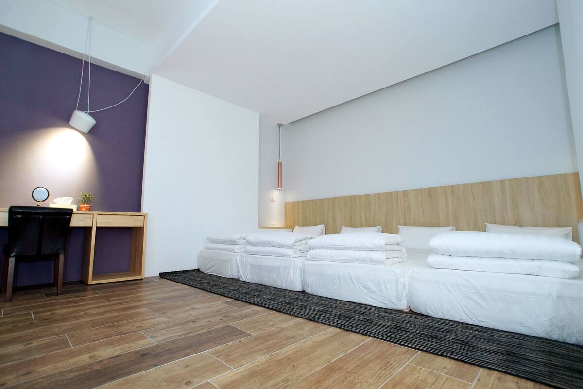 Una habitación de hotel moderna con un escritorio de madera, una silla, una cama con ropa blanca y un espejo grande.