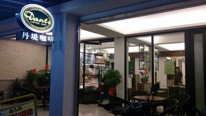 L’extérieur d’un café, avec une enseigne indiquant « Dan’s Coffee Shop » et une enseigne au néon au-dessus.