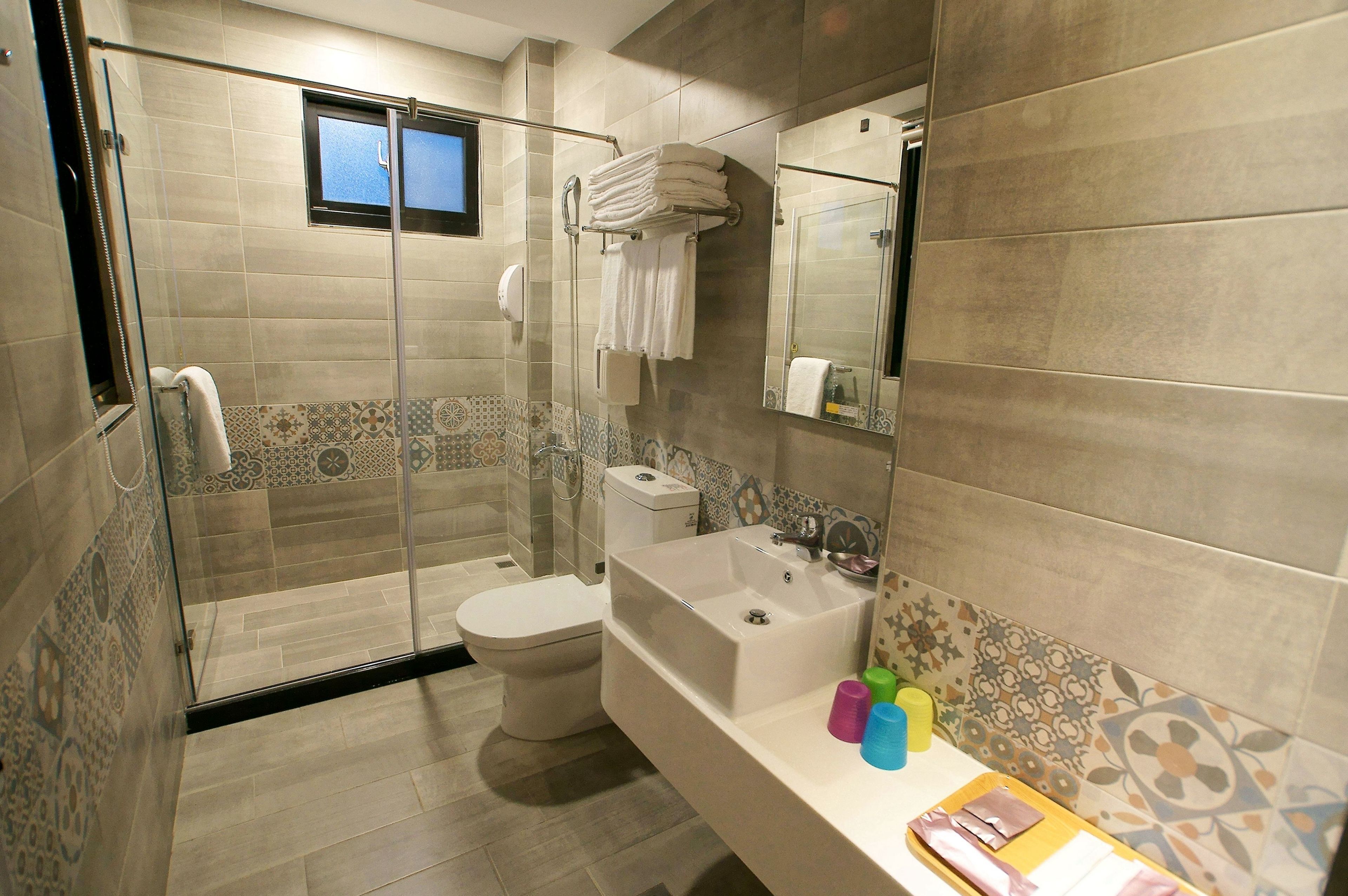 A modern bathroom with a glass-enclosed shower, a toilet, a bathtub, and a vanity with toiletries.