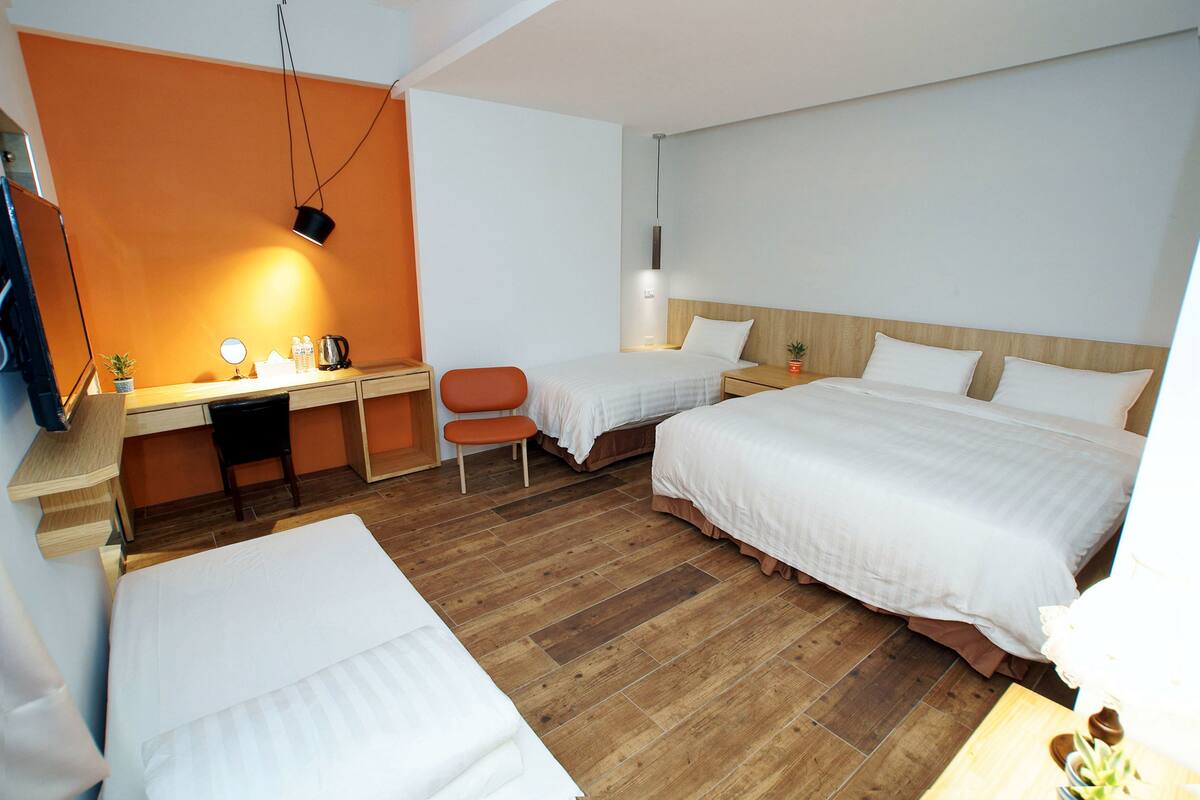 Habitación de hotel con dos camas, un escritorio, una silla y una mesita de noche con lámpara.