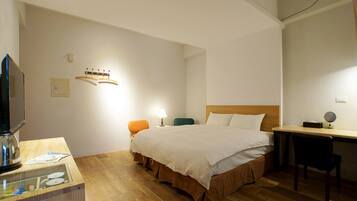 A hotel room with a bed, a desk, a chair, a television, and a small table with a lamp.
