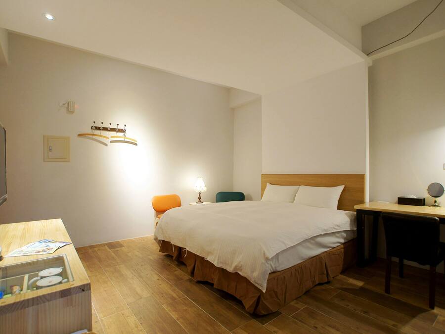 A hotel room with a bed, a desk, a chair, a television, and a small table with a lamp.