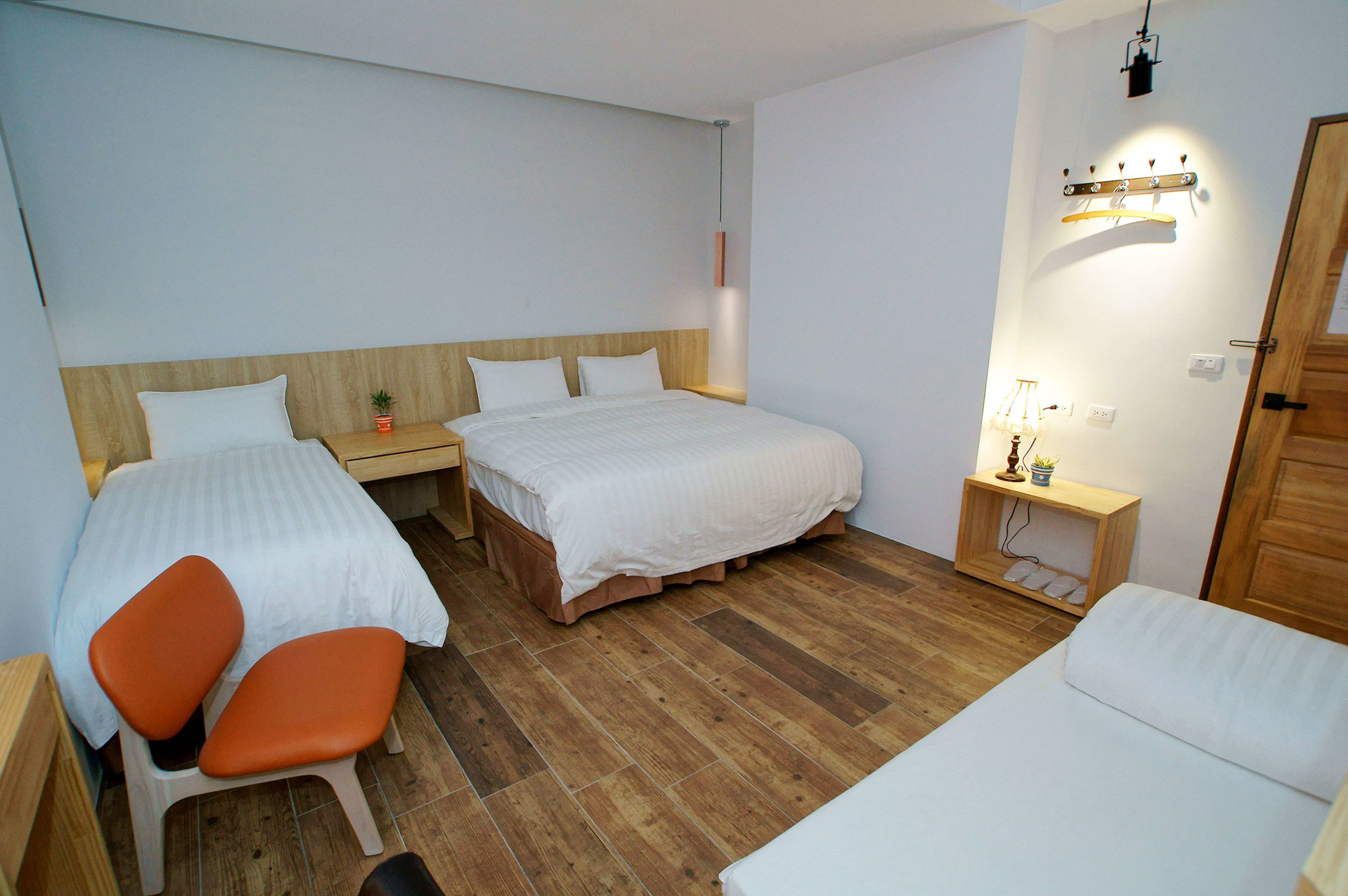 A room with two beds, a chair, a small table, and a bedside table with a lamp.