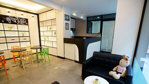 Un hall d’hôtel moderne comprenant un espace salon, un comptoir d’accueil et donnant sur la cuisine.