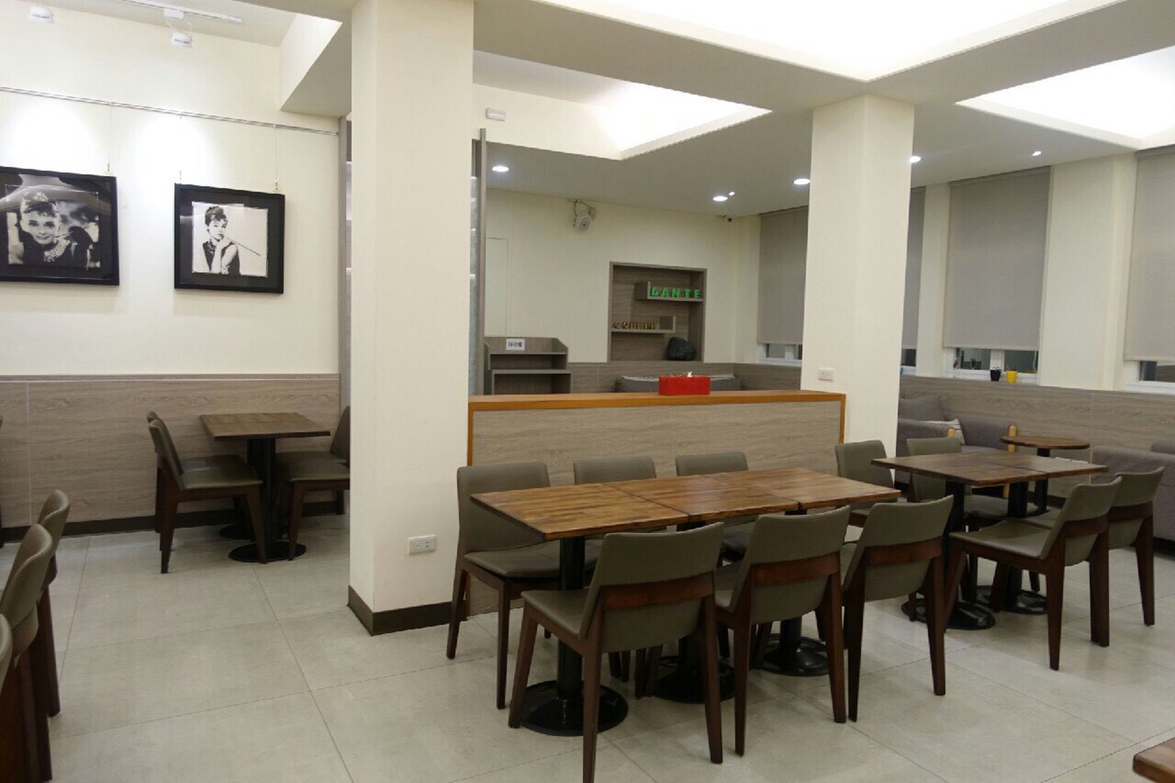 A modern dining area with multiple tables and chairs, a counter with a red object, and framed pictures on the wall.