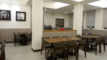 A modern dining area with multiple tables and chairs, a counter with a red object, and framed pictures on the wall.