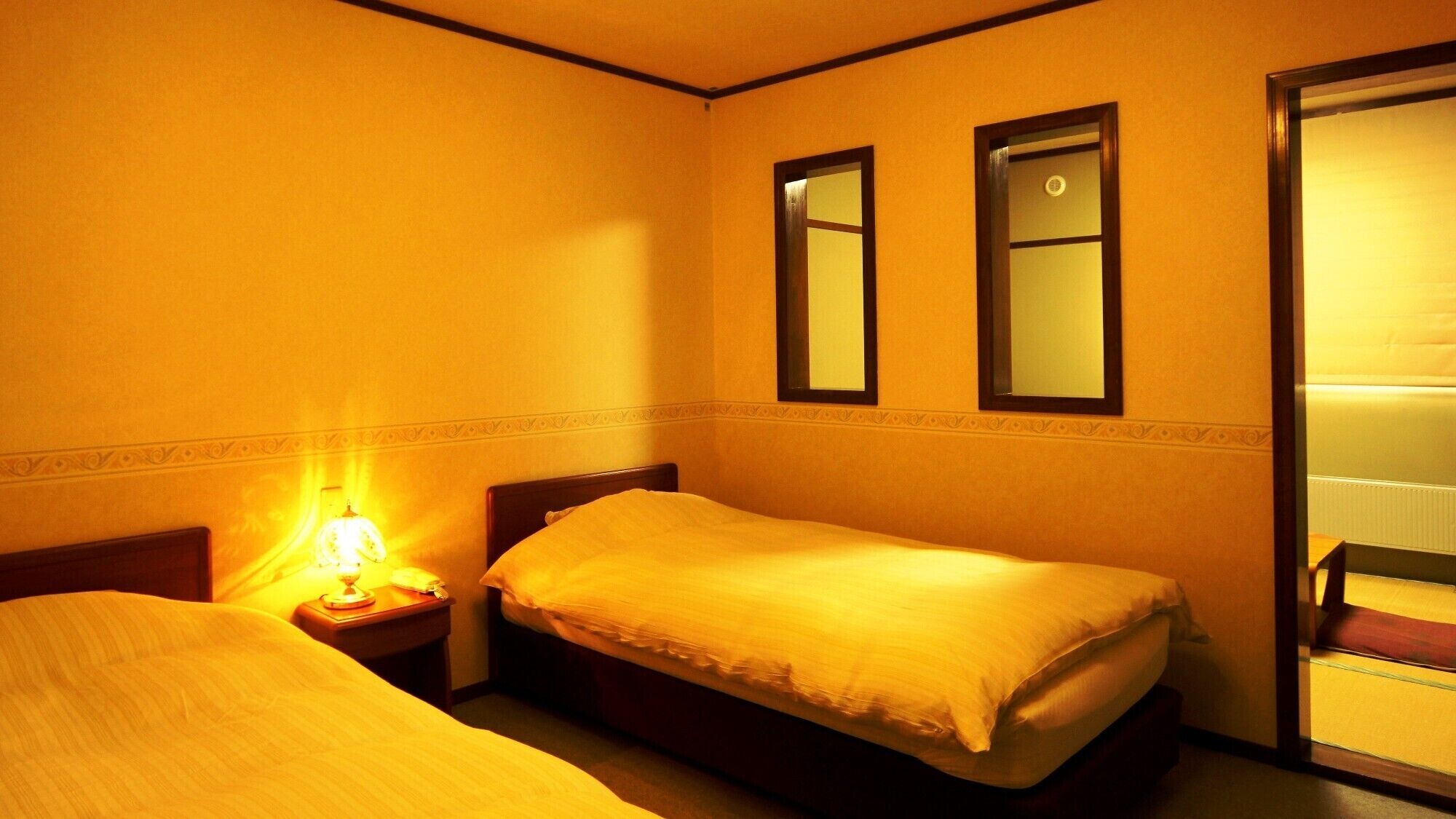 A hotel room with two beds, a bedside lamp, and a mirror on the wall.