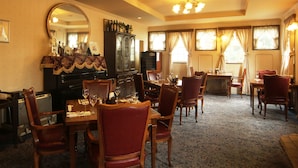 A formal dining room with a long table, multiple chairs, a grand piano, a large mirror, and a cabinet with bottles.