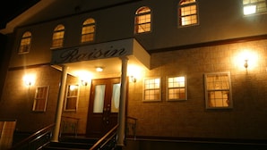 A building with a sign reading "Raisin" above the entrance, featuring a staircase, multiple windows with lights, and a brick facade.
