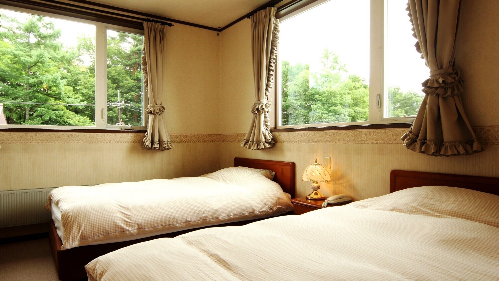 A hotel room with two beds, a nightstand with a lamp, and a window with curtains.