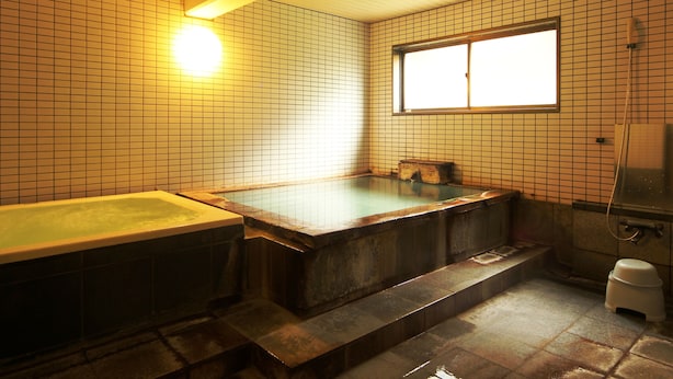 A traditional Japanese-style bathroom with a wooden bathtub, a window, and tiled walls.