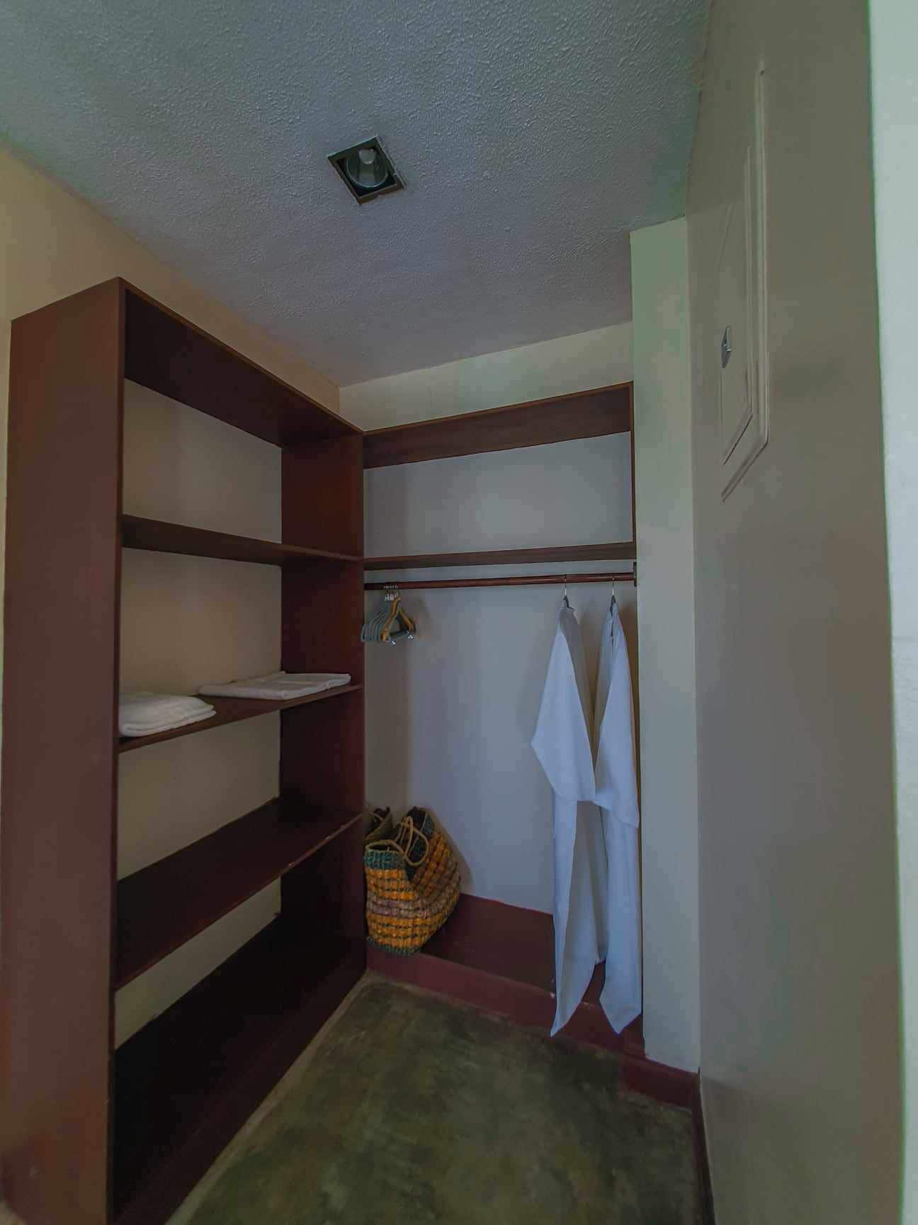 A small, enclosed bathroom with wooden shelves, a towel rack, and a shower area.
