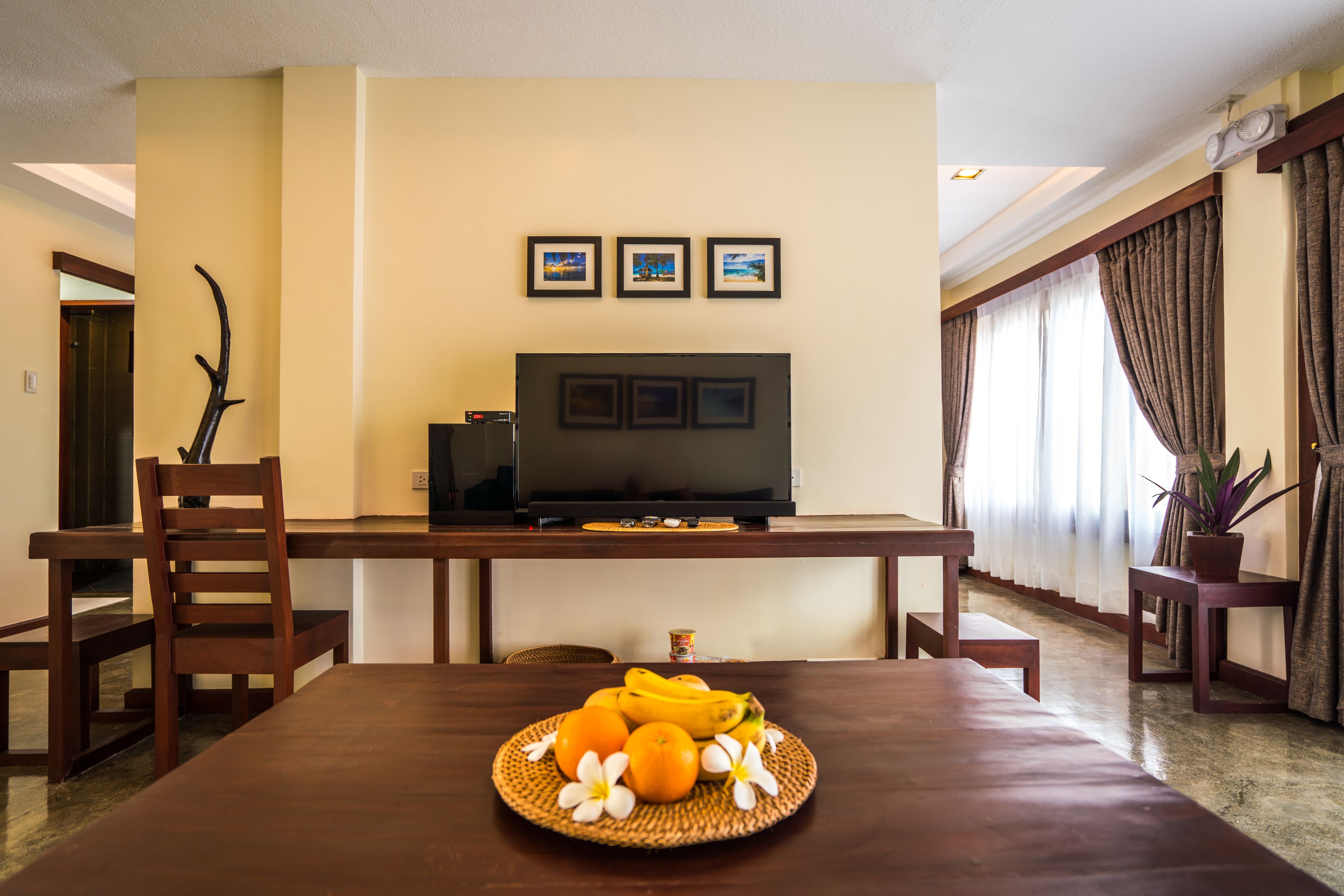 A dining area with a wooden table, chairs, a television, and a fruit basket.