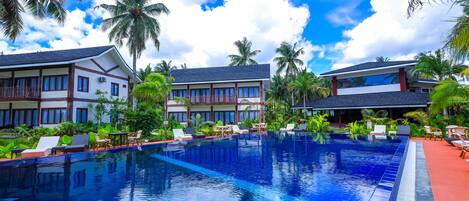 A swimming pool with lounge chairs and palm trees, surrounded by a hotel building with balconies.