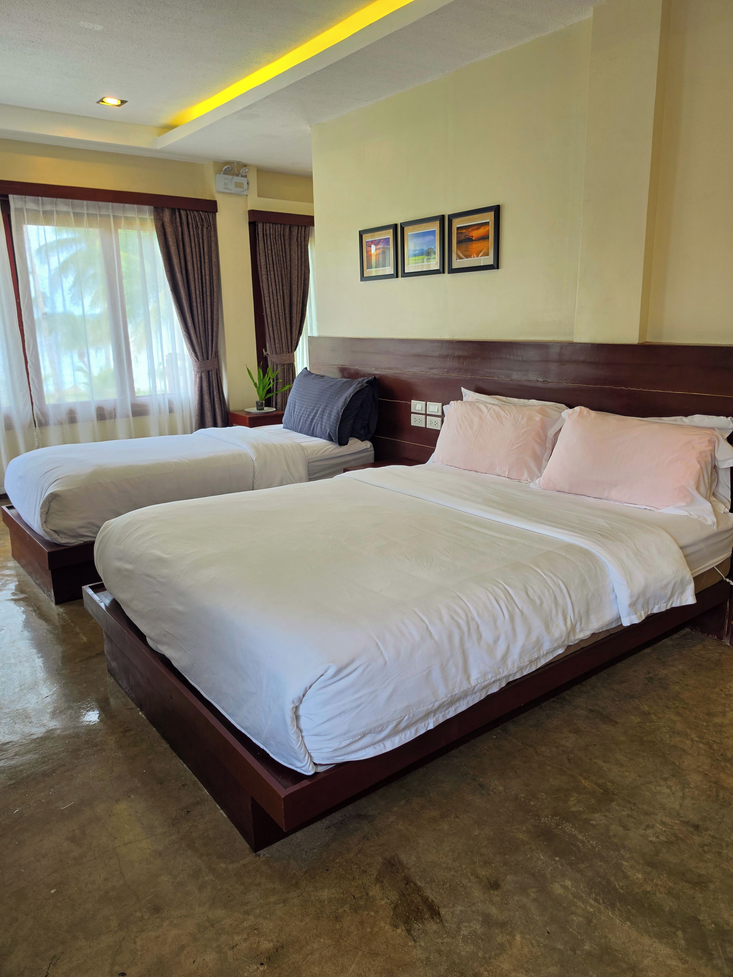 A hotel room with two beds, a wooden headboard, a ceiling light, and a window with curtains.