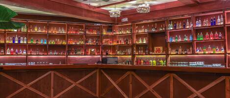 Zona de bar con varias estanterías llenas de botellas de licor, una barra de madera y ventiladores de techo.