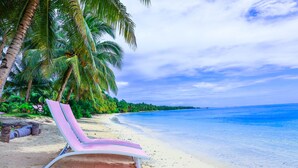 A beach with a pink lounge chair, palm trees, and clear blue water. - Retreat Siargao Resort (General Luna)