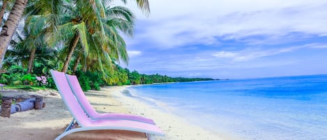 A beach with a pink lounge chair, palm trees, and clear blue water.