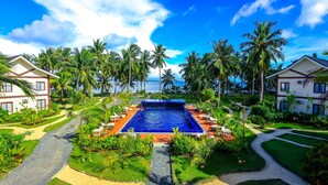 A resort with a central swimming pool, palm trees, and a view of the ocean. - Retreat Siargao Resort (General Luna)