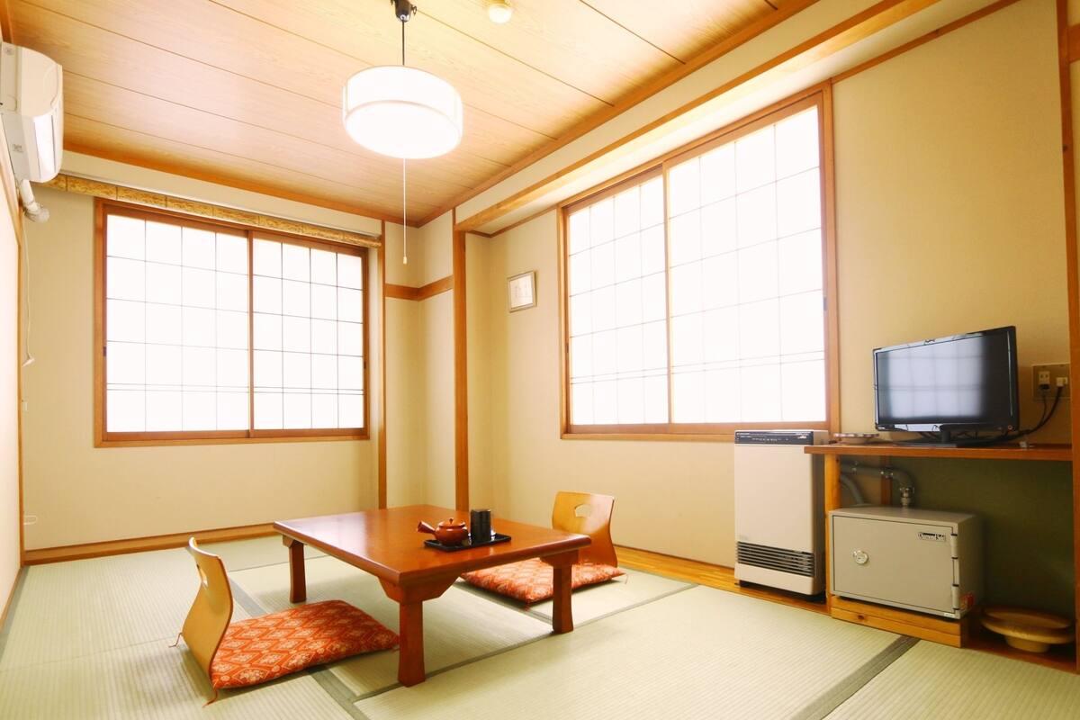 Ett traditionellt japanskt rum med tatamimattor på golvet, ett lågt bord med kuddar, en tv och en värmare.