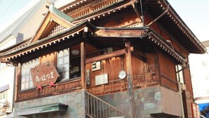 A traditional wooden building with a stone facade, wooden stairs, and a sign with Japanese characters. - Kawatatsu (Nozawaonsen)