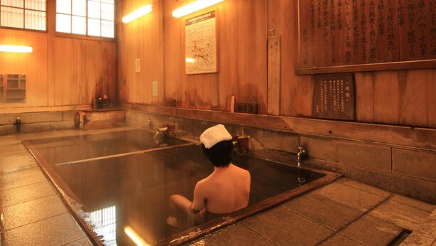 A traditional Japanese onsen with wooden walls and a large hot spring bath. - Kawatatsu (Nozawaonsen)