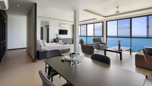 A modern hotel room with a large window offering a sea view, a dining area with a table and chairs, a sofa, and a bed with a white headboard. - Ban Nai Fan (Koh Samui)