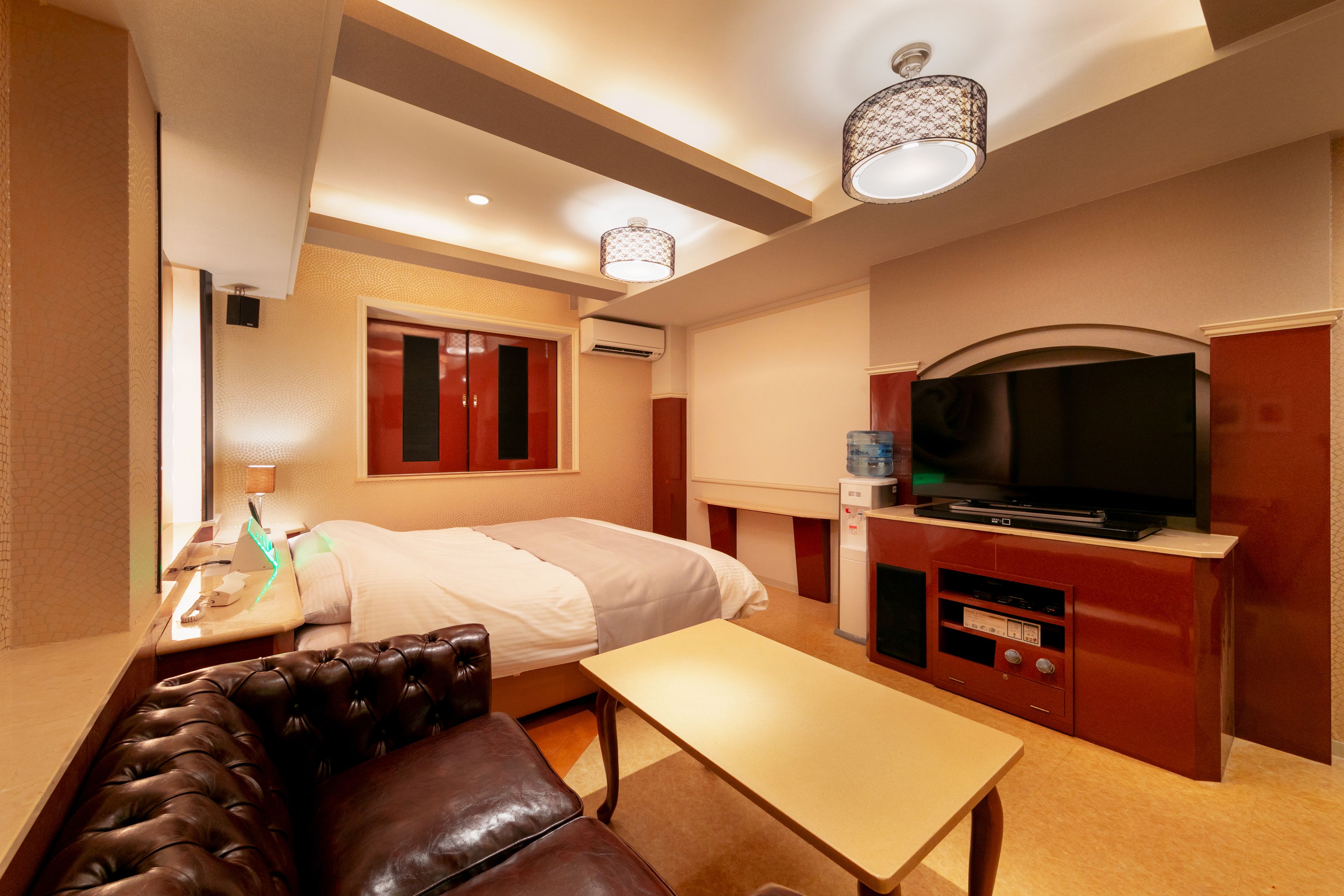 Una habitació d'hotel amb llit, televisió, escriptori, sofà de cuir i un dispensador d'aigua.