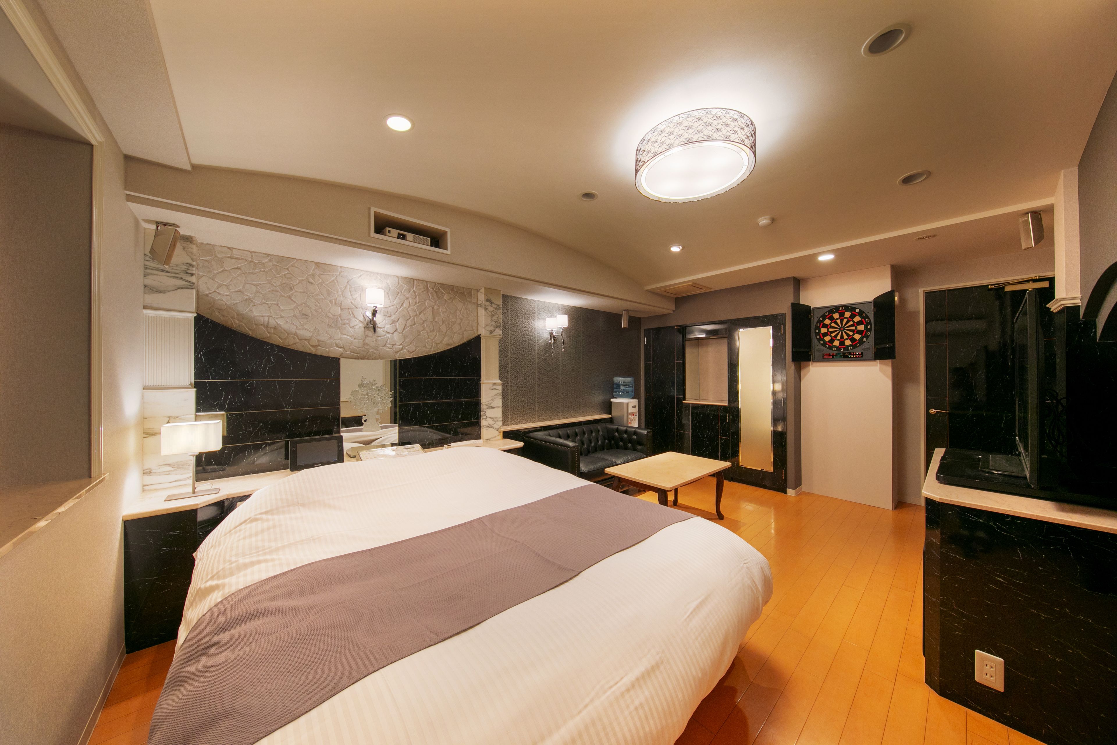 A modern hotel room with a large bed, a desk, a mirror, a shower area, and a TV.