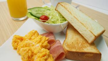 A breakfast plate with scrambled eggs, ham, toast, a salad, and a glass of orange juice.