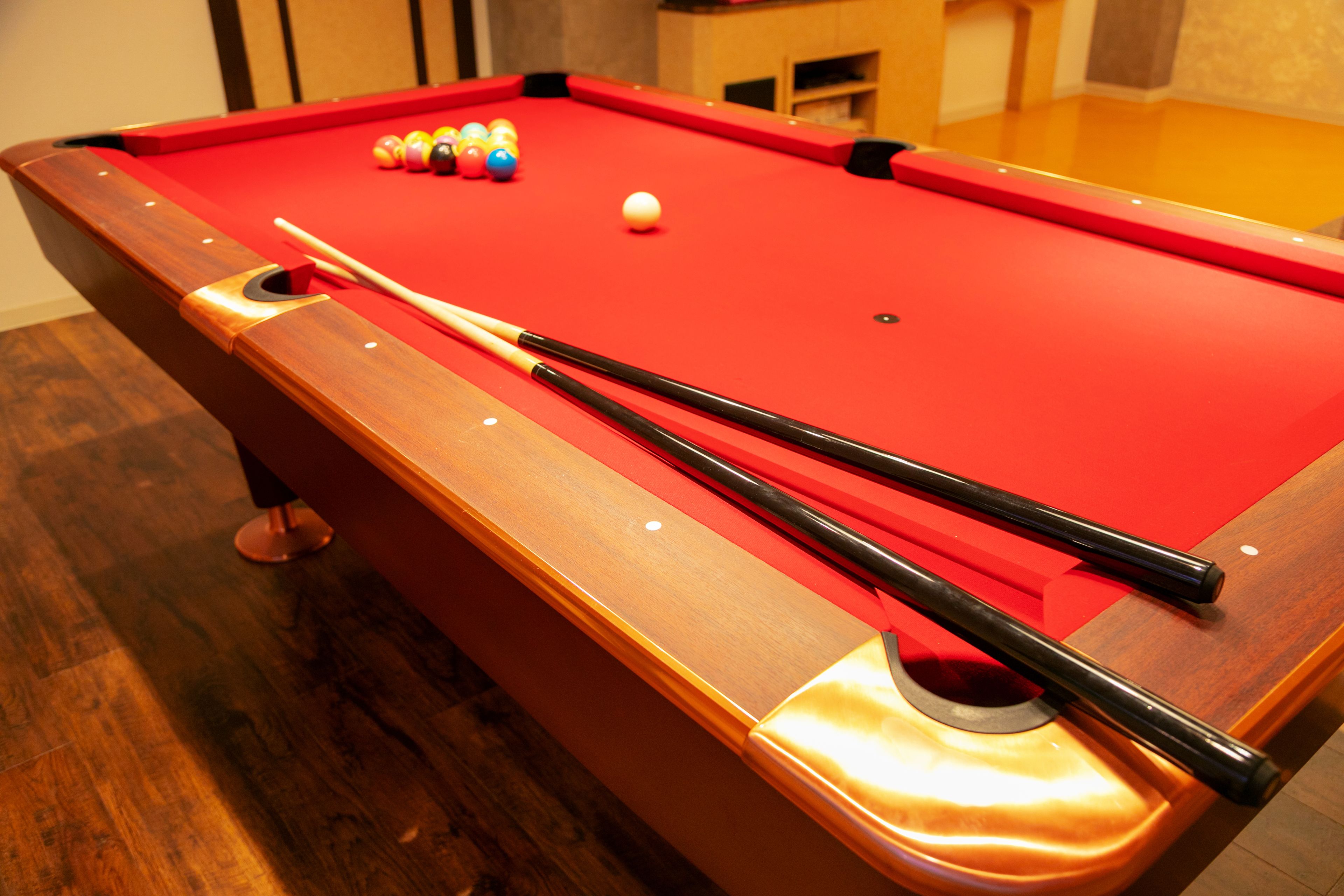 Une table de billard recouverte d’un feutre rouge, avec des queues de billard et des billes de couleurs vives.