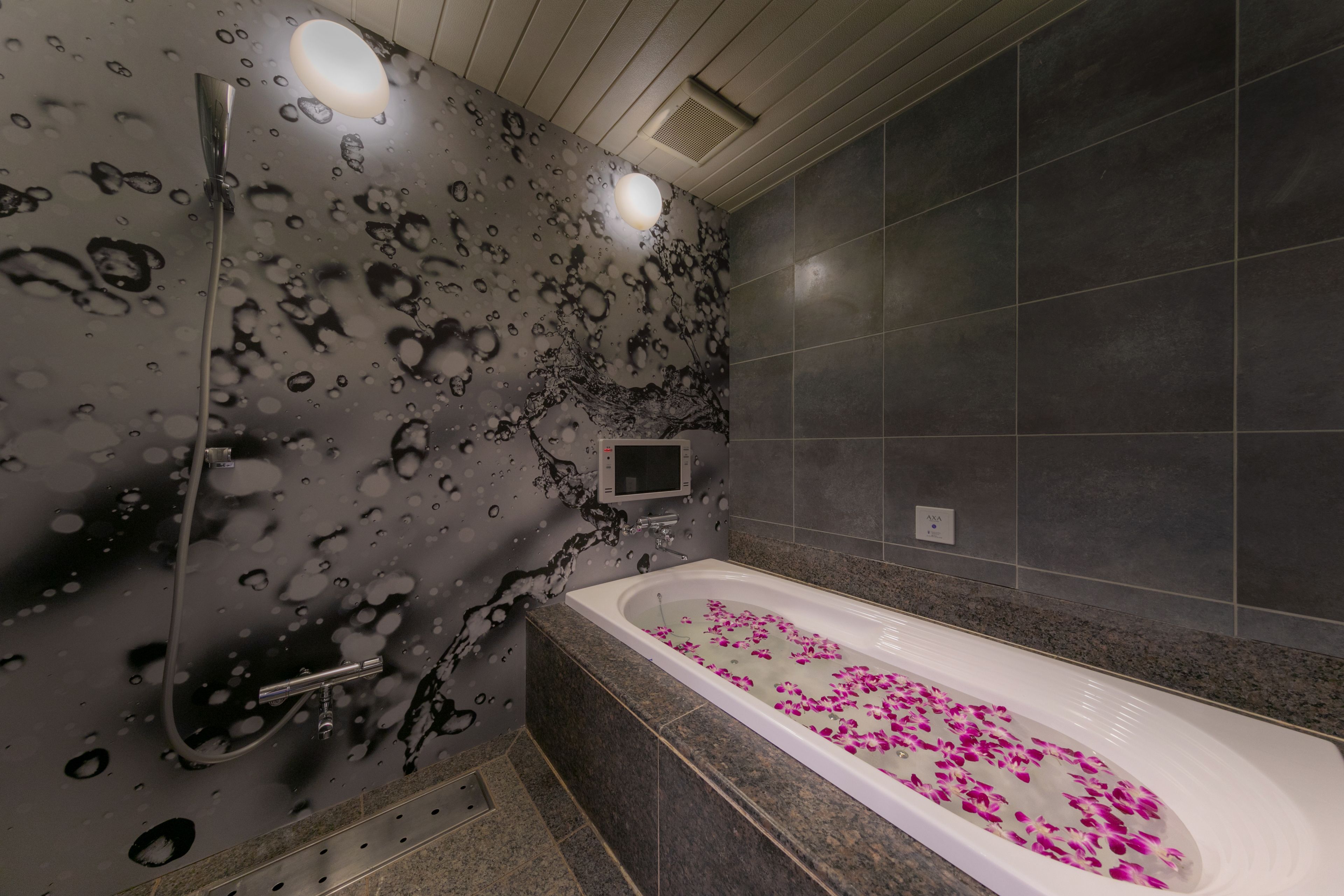 Un bagno moderno con una vasca da bagno piena di petali di rosa, una doccia con porta in vetro e una parete con un motivo originale in bianco e nero.