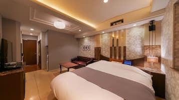 Une chambre d’hôtel dotée d’un grand lit, d’un bureau avec un ordinateur, d’un coin salon avec un canapé et un fauteuil, et d’une salle de bain visible à travers une porte ouverte.