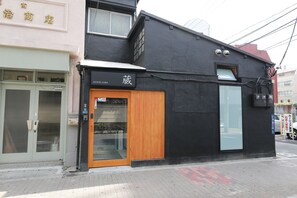 A building with a black facade, a wooden door, and a sign that reads "HOSTEL KURA".