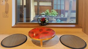 A room with a wooden floor, a round table with a red and black patterned top, and two black mats on either side. - Hostel Kura (Tokyo)