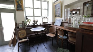 A cozy corner with a wooden table, wicker chairs, a small window with a view, and a chalkboard menu. - Hostel Kura (Tokyo)