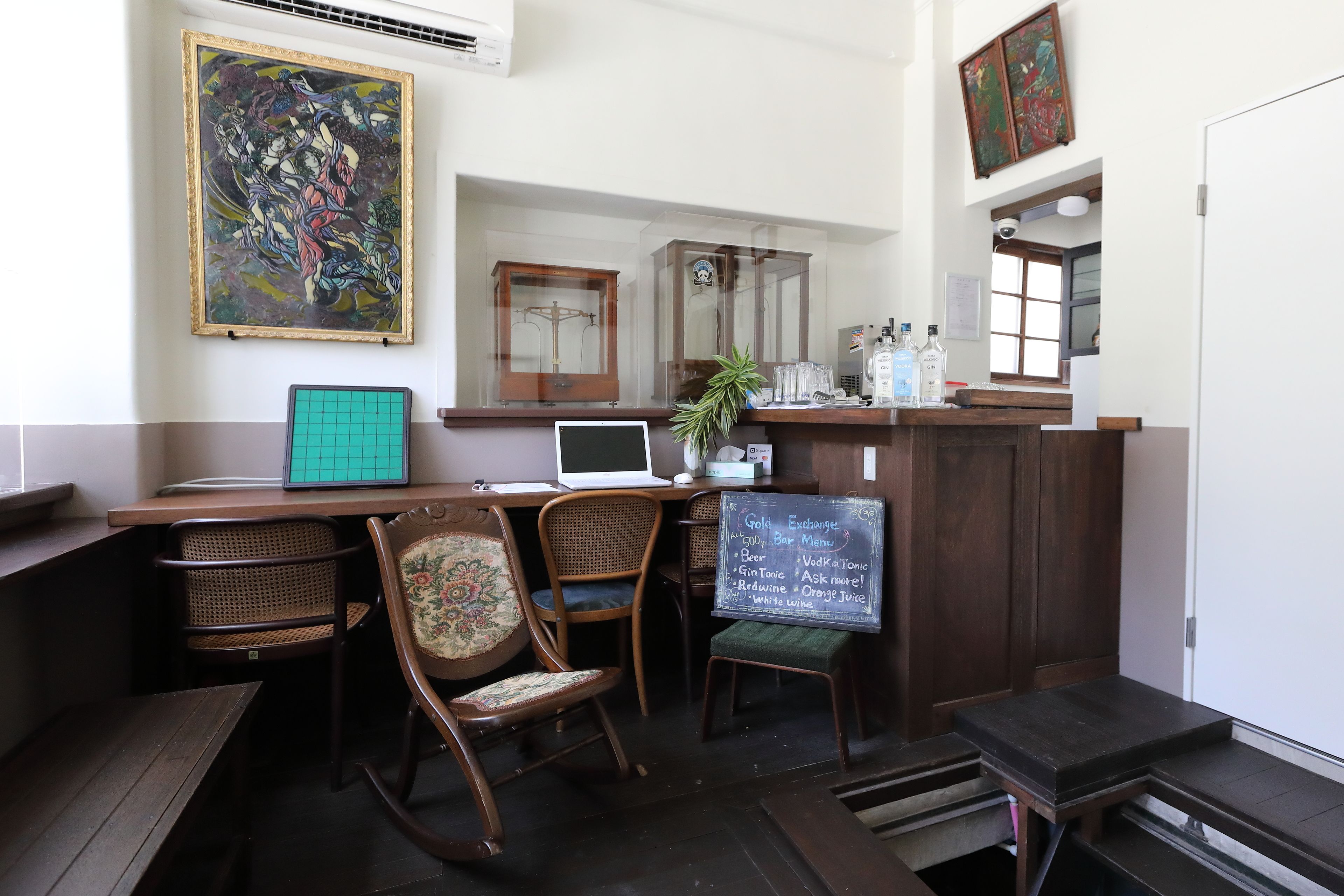 Zona de bar con muebles de madera, un menú en una pizarra y obras de arte en las paredes.
